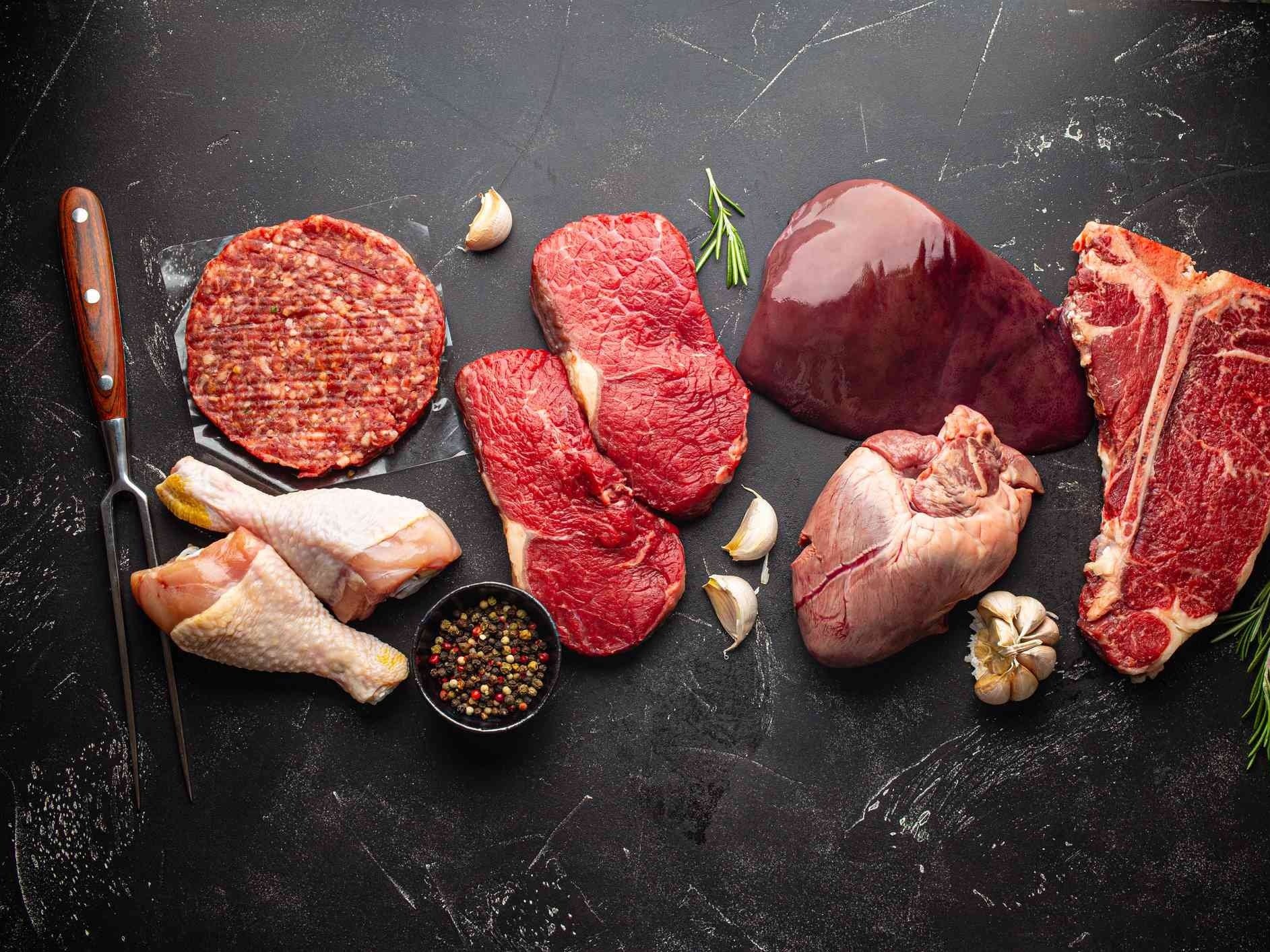 Assorted cuts of raw beef, including ribeye and tenderloin, displayed on a wooden cutting board with fresh rosemary, a mortar and pestle, and a bowl of sea salt, highlighting gourmet cooking ingredients.